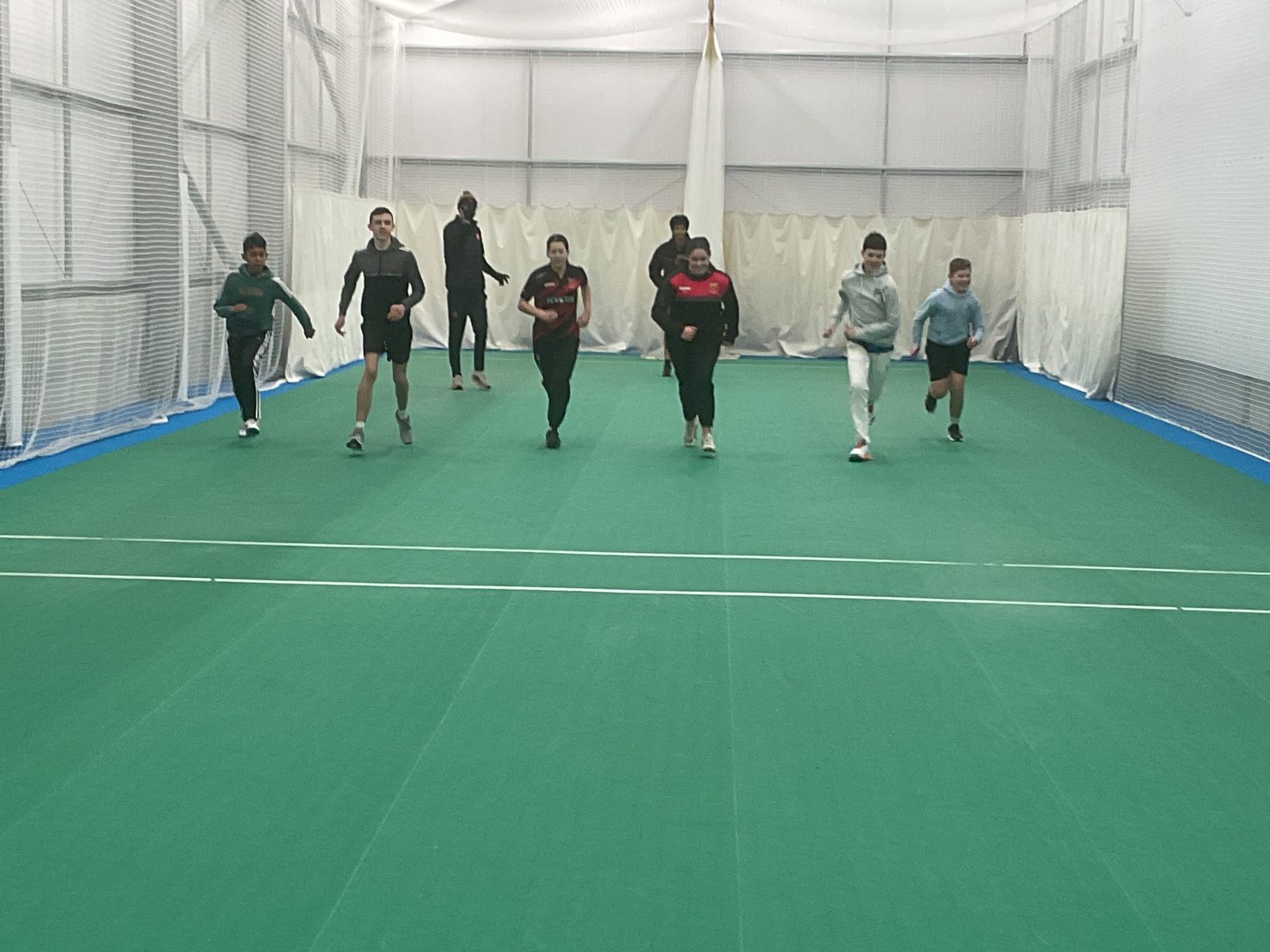 Academy players jogging towards the camera during a warm-up in an indoor netted hall