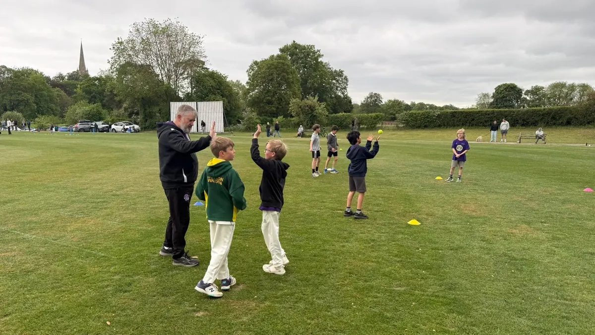 Centurion coach Bryan McManus high-fiving a young player on an outdoor field during junior fielding drills