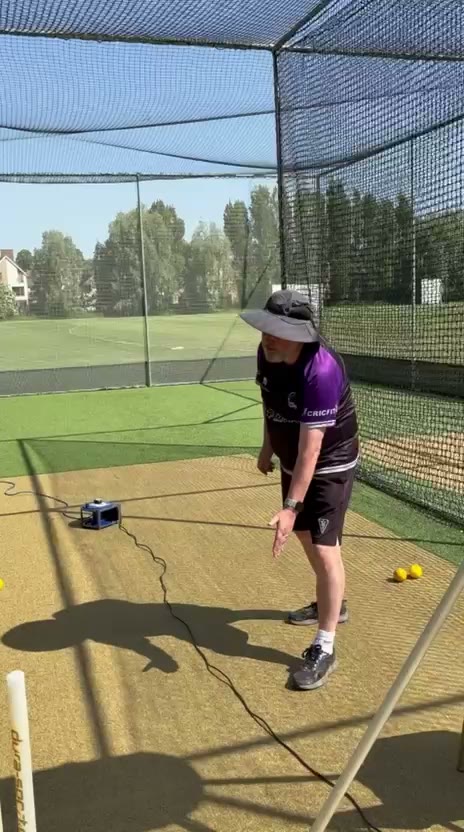 Centurion coach at a bowling machine in an outdoor net on a sunny day, batter at the far end